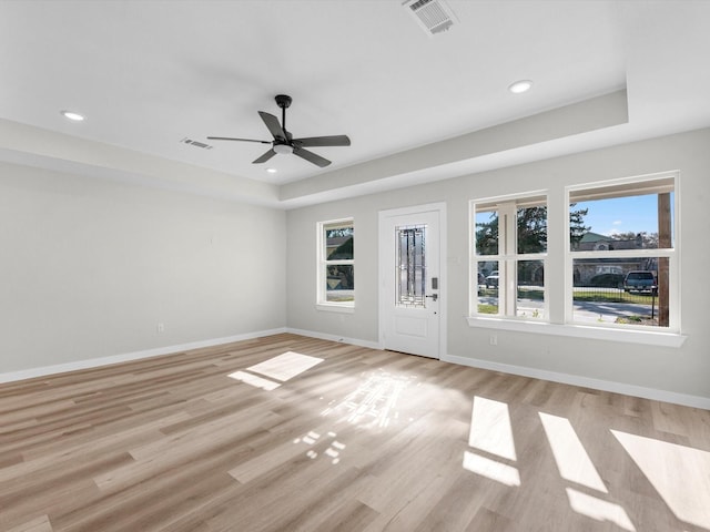 unfurnished room featuring ceiling fan, a tray ceiling, and light wood-type flooring