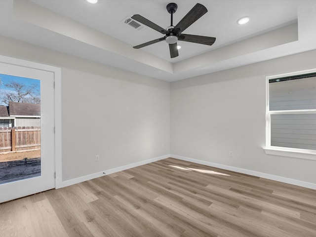 unfurnished room with light wood-type flooring, ceiling fan, and a raised ceiling