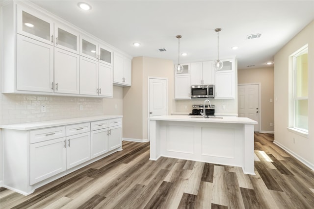 kitchen with a center island with sink, hanging light fixtures, stainless steel appliances, white cabinets, and dark hardwood / wood-style flooring