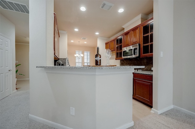 kitchen featuring decorative light fixtures, backsplash, kitchen peninsula, an inviting chandelier, and light carpet