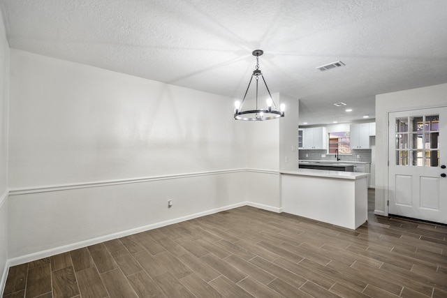 unfurnished dining area with a textured ceiling, sink, and a notable chandelier