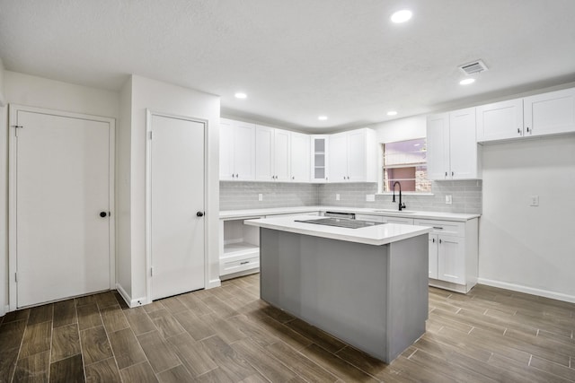 kitchen with white cabinets, a kitchen island, black electric stovetop, tasteful backsplash, and sink