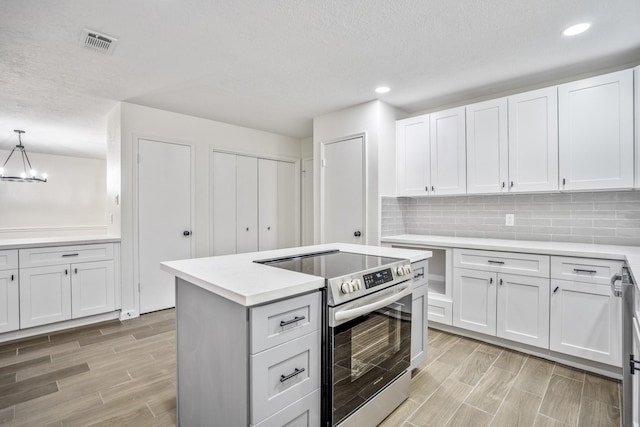 kitchen with white cabinets, stainless steel range with electric cooktop, an inviting chandelier, decorative backsplash, and hanging light fixtures