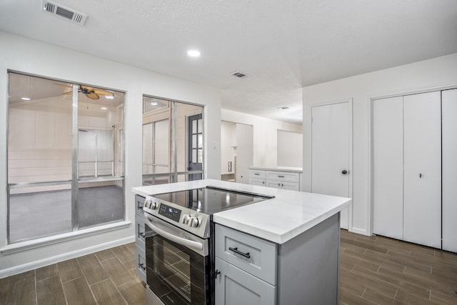 kitchen with stainless steel range with electric stovetop, ceiling fan, gray cabinetry, a textured ceiling, and a center island