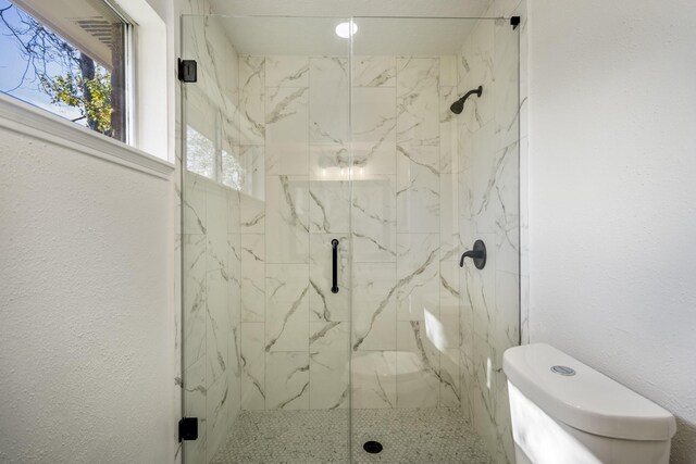 bathroom featuring a shower with shower door and toilet