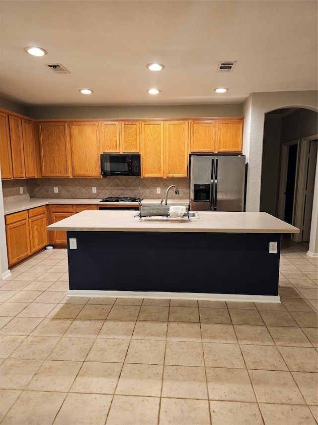 kitchen featuring light tile patterned floors, stainless steel refrigerator with ice dispenser, and an island with sink