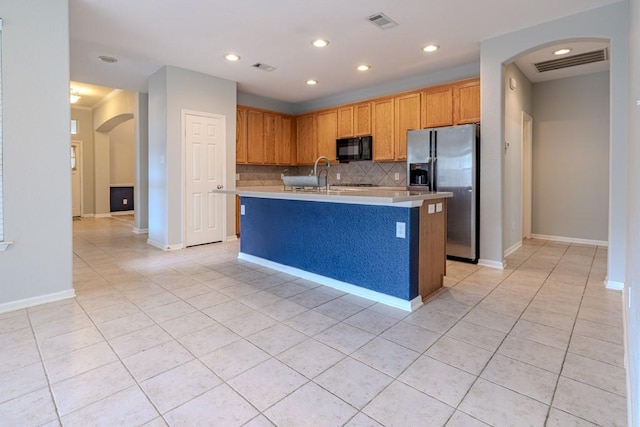 kitchen featuring tasteful backsplash, an island with sink, light tile patterned flooring, and stainless steel fridge with ice dispenser