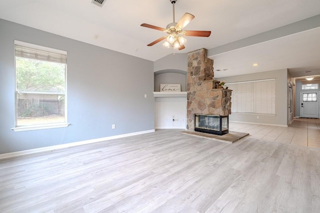 unfurnished living room with ceiling fan, lofted ceiling, light hardwood / wood-style floors, and a stone fireplace