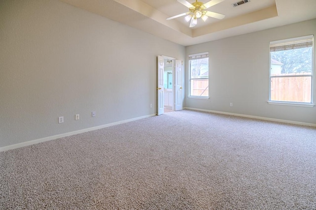 carpeted spare room with a raised ceiling and ceiling fan