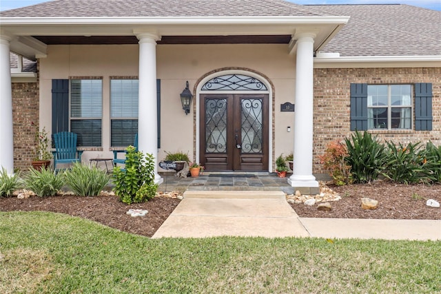 entrance to property with a shingled roof, covered porch, and brick siding