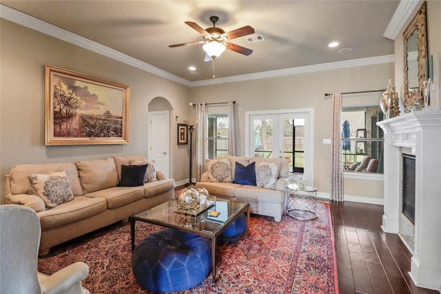 living room featuring arched walkways, dark wood-style flooring, baseboards, a glass covered fireplace, and crown molding