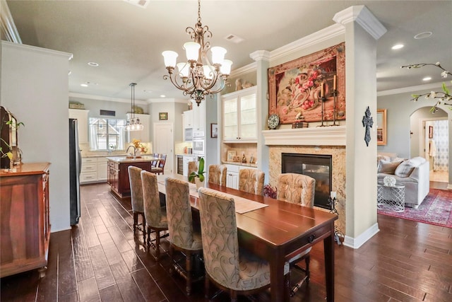 dining space with dark wood-style floors, arched walkways, crown molding, and an inviting chandelier