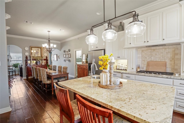 kitchen featuring arched walkways, a kitchen island with sink, stainless steel appliances, white cabinetry, and pendant lighting