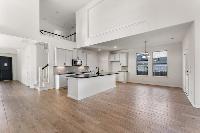 kitchen with light hardwood / wood-style floors, white cabinetry, a center island with sink, and hanging light fixtures