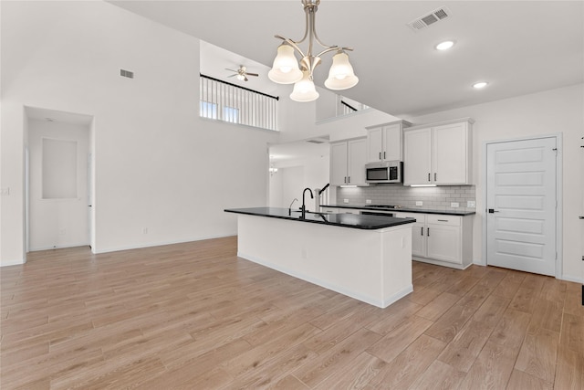 kitchen with tasteful backsplash, white cabinets, pendant lighting, light hardwood / wood-style floors, and a high ceiling