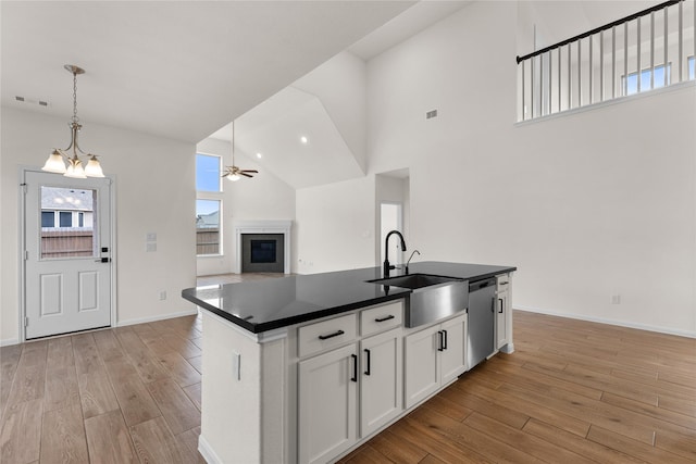 kitchen featuring an island with sink, hanging light fixtures, stainless steel dishwasher, white cabinets, and sink