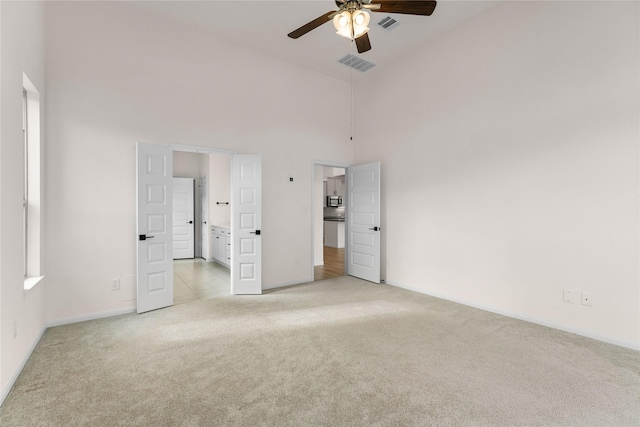 unfurnished bedroom with ceiling fan, ensuite bath, light carpet, and a towering ceiling