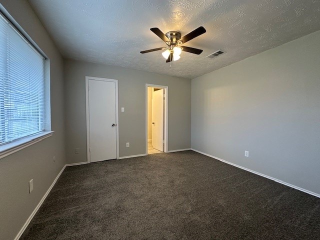 empty room featuring a textured ceiling, ceiling fan, and dark carpet