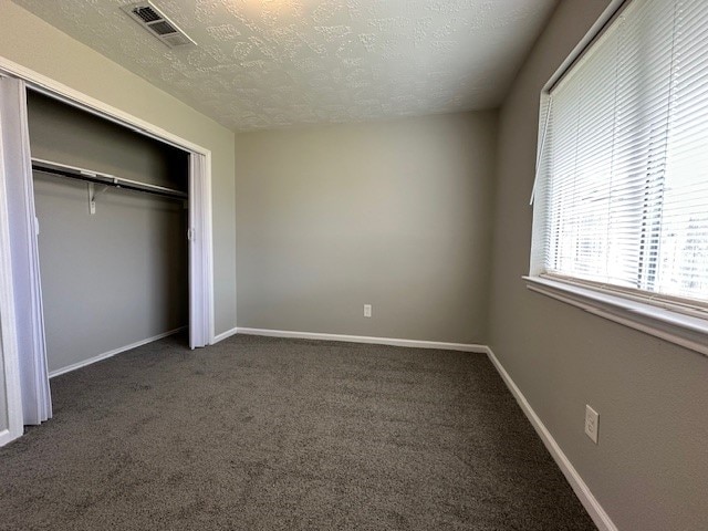 unfurnished bedroom featuring a closet, a textured ceiling, and dark colored carpet