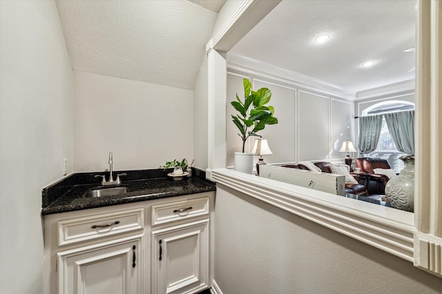 bar with sink, white cabinetry, a textured ceiling, and dark stone counters