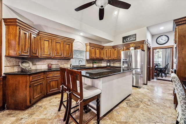 kitchen with dark stone countertops, decorative backsplash, sink, stainless steel fridge, and ceiling fan