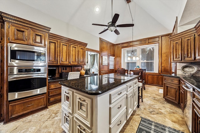 kitchen featuring lofted ceiling, dark stone countertops, a kitchen island, appliances with stainless steel finishes, and ceiling fan with notable chandelier