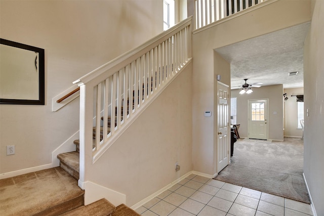 stairs with ceiling fan, a textured ceiling, carpet, and a high ceiling