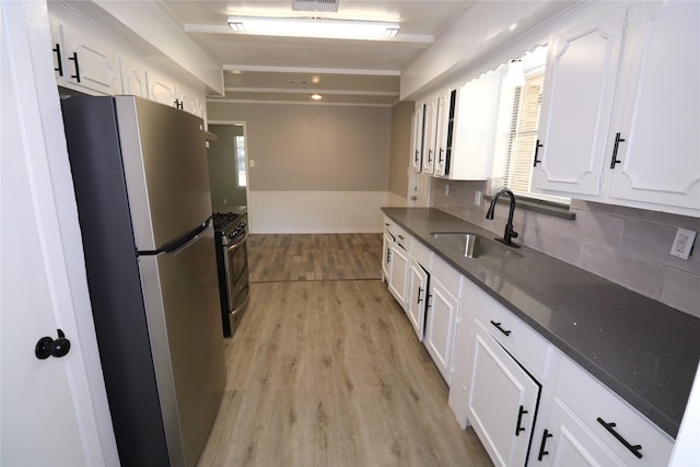 kitchen featuring appliances with stainless steel finishes, sink, light wood-type flooring, white cabinets, and beamed ceiling