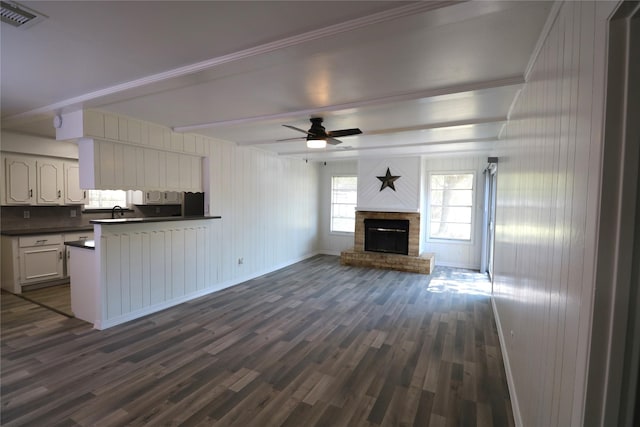 unfurnished living room featuring ceiling fan, a fireplace, dark hardwood / wood-style floors, beamed ceiling, and crown molding