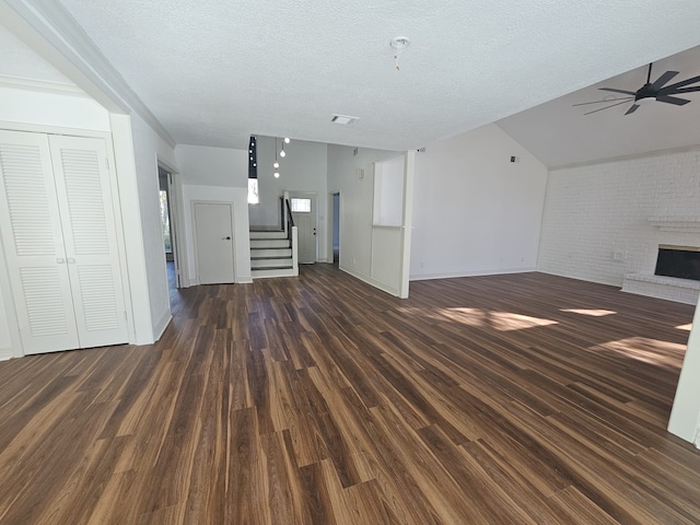 unfurnished living room featuring a brick fireplace, ceiling fan, vaulted ceiling, dark wood-type flooring, and a textured ceiling