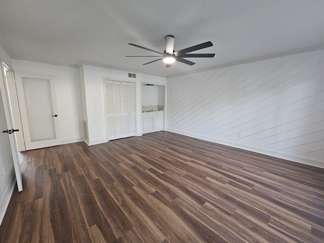 unfurnished bedroom with ceiling fan, dark hardwood / wood-style flooring, wood walls, and crown molding