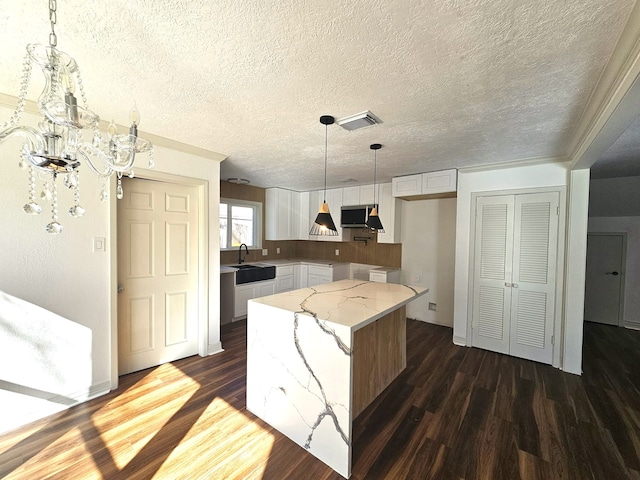 kitchen featuring pendant lighting, white cabinets, a center island, extractor fan, and light stone counters