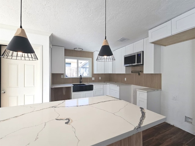 kitchen featuring white cabinetry, light stone countertops, pendant lighting, and sink