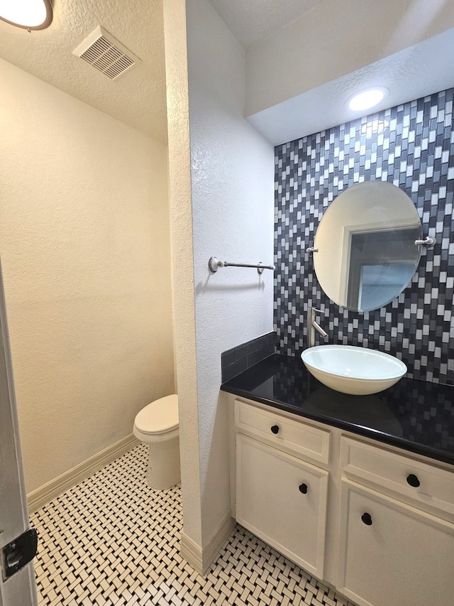 bathroom featuring toilet, decorative backsplash, tile patterned flooring, a textured ceiling, and vanity