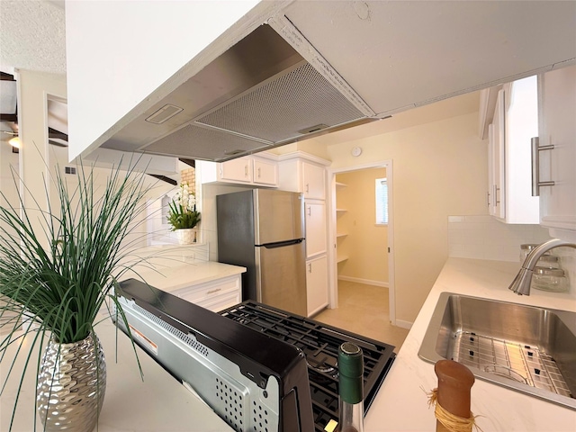 kitchen with sink, white cabinets, range hood, and stainless steel refrigerator