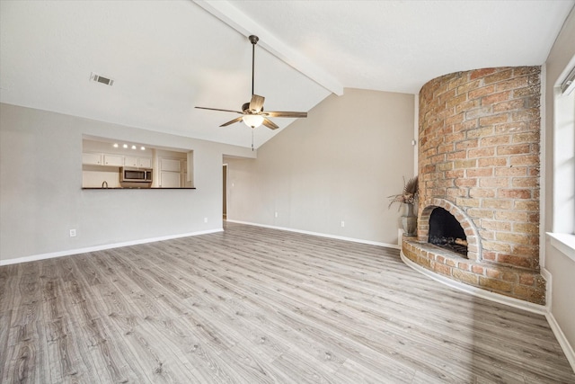 unfurnished living room with ceiling fan, light hardwood / wood-style floors, lofted ceiling with beams, and a brick fireplace