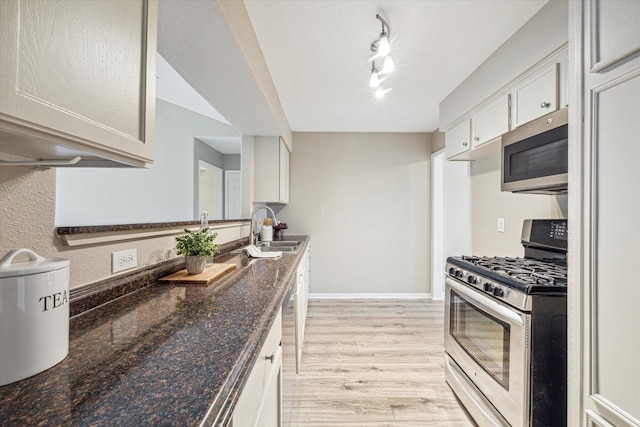 kitchen with sink, light hardwood / wood-style flooring, appliances with stainless steel finishes, track lighting, and dark stone counters