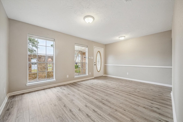 empty room with a textured ceiling and light hardwood / wood-style flooring