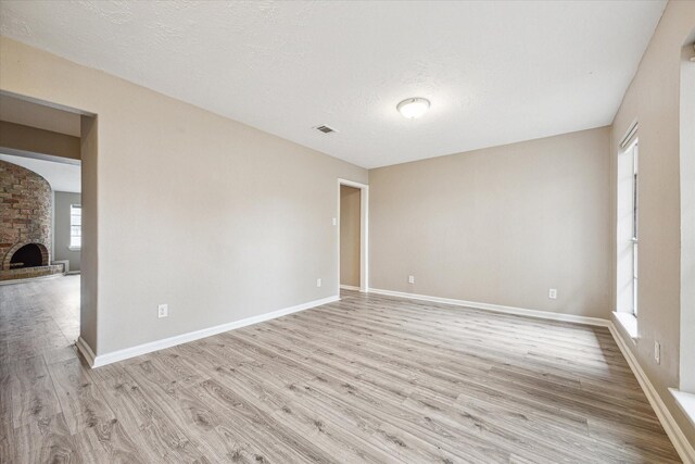 unfurnished room with a fireplace, a textured ceiling, and light hardwood / wood-style flooring