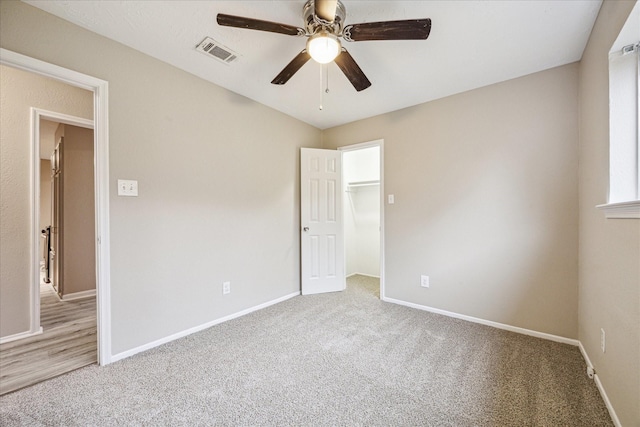 unfurnished bedroom featuring ceiling fan, light carpet, a spacious closet, and a closet