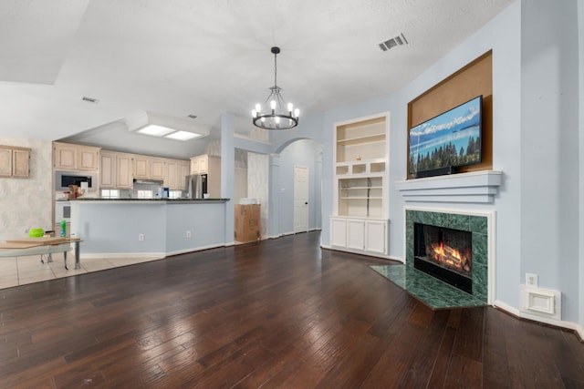 unfurnished living room featuring a premium fireplace, hardwood / wood-style flooring, a textured ceiling, built in shelves, and a chandelier