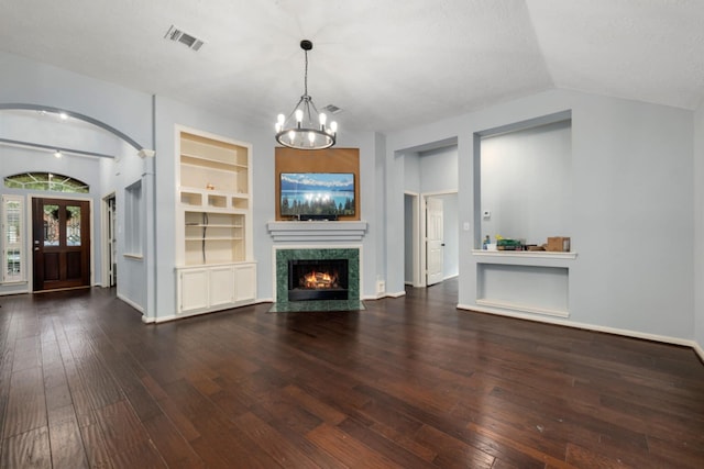 unfurnished living room with lofted ceiling, dark hardwood / wood-style floors, a premium fireplace, an inviting chandelier, and built in shelves