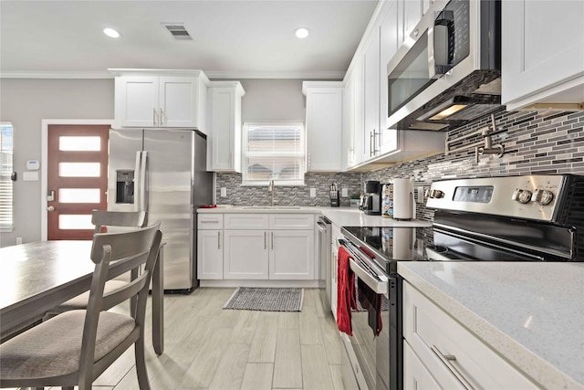 kitchen with appliances with stainless steel finishes, light stone countertops, ornamental molding, white cabinets, and sink