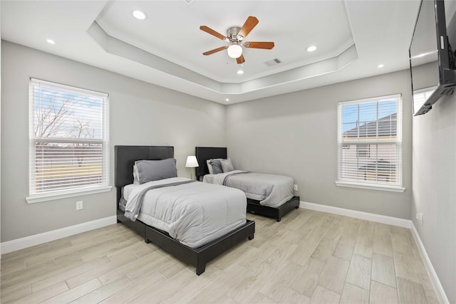 bedroom featuring ceiling fan, light hardwood / wood-style floors, a tray ceiling, and multiple windows