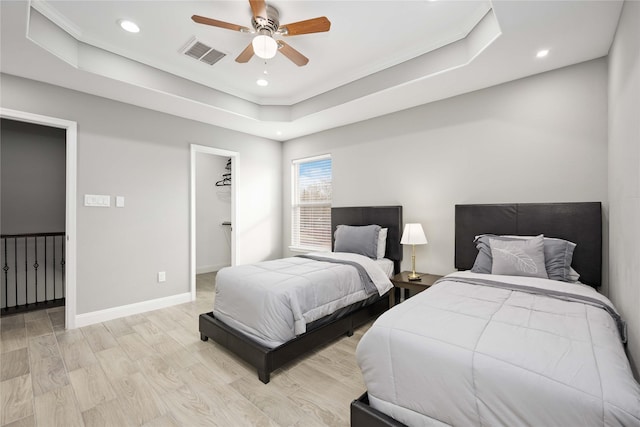 bedroom featuring ceiling fan, light hardwood / wood-style floors, a raised ceiling, a walk in closet, and a closet