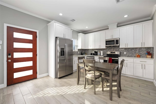 kitchen with appliances with stainless steel finishes, ornamental molding, white cabinets, and sink