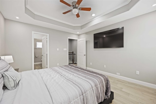 bedroom featuring ceiling fan, light hardwood / wood-style flooring, a tray ceiling, and ensuite bath