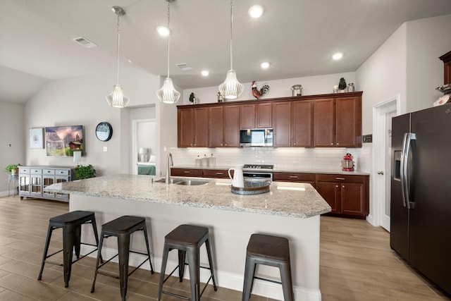 kitchen with appliances with stainless steel finishes, decorative light fixtures, an island with sink, sink, and a breakfast bar