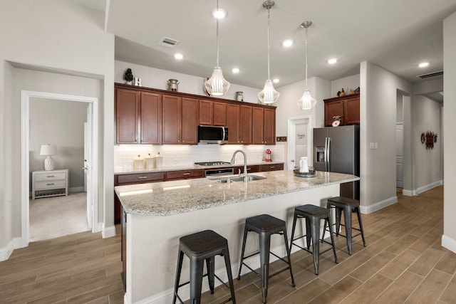 kitchen featuring stainless steel appliances, sink, hanging light fixtures, a kitchen breakfast bar, and a kitchen island with sink