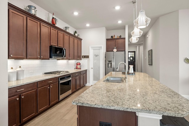 kitchen with appliances with stainless steel finishes, a center island with sink, hanging light fixtures, and sink